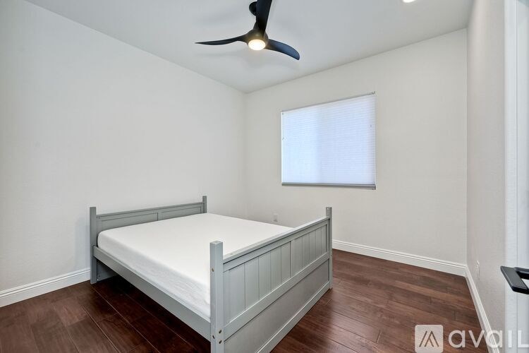 A bedroom with a bed, wooden floors, and a ceiling fan.