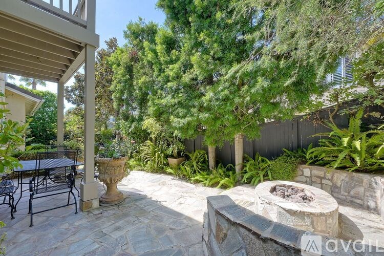 A patio with a table and chairs is surrounded by greenery.