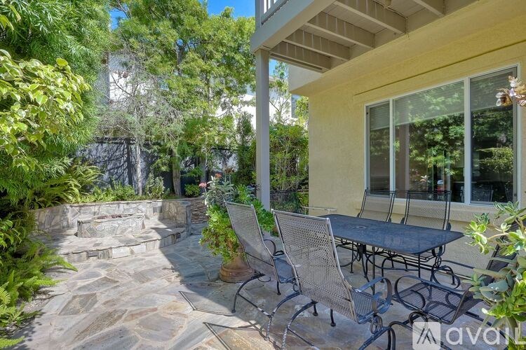 A patio with a table and chairs is surrounded by greenery.