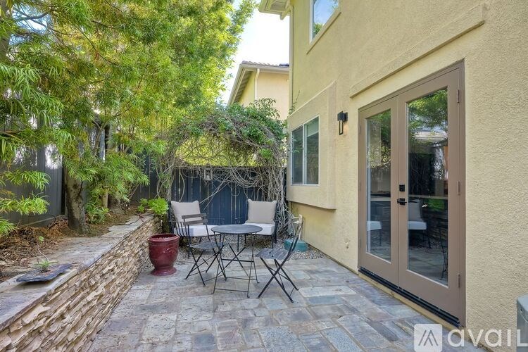 A patio with a table and chairs is surrounded by a stone wall and trees.