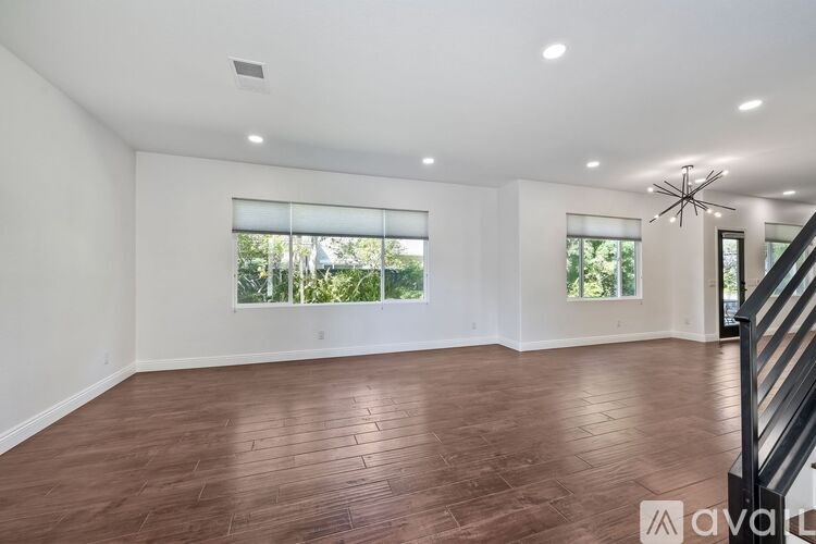 A spacious room with wooden flooring and a staircase on the right side.