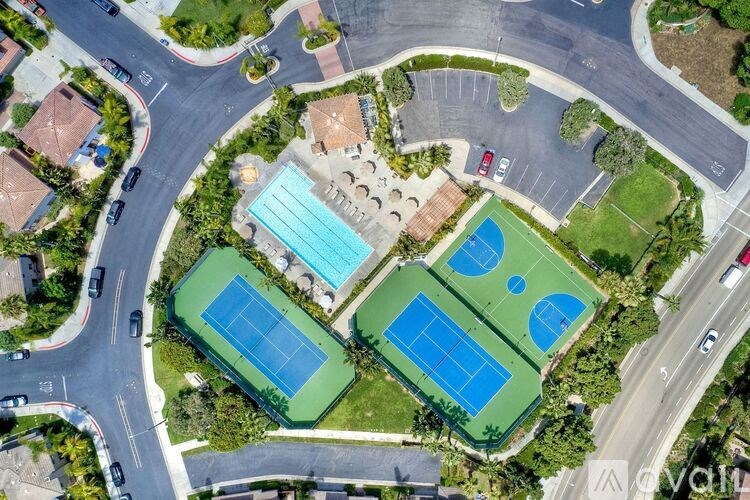 An aerial view of a tennis court surrounded by a parking lot and residential area.