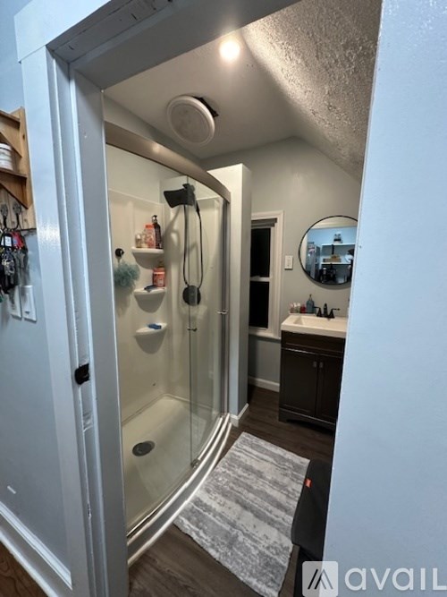 A bathroom with a glass shower door and a round mirror on the wall.
