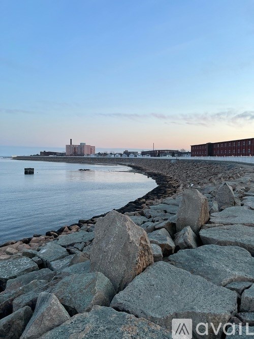 A rocky shoreline with a body of water and a building in the distance.
