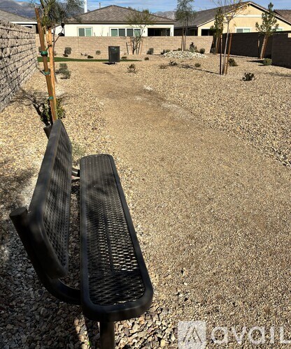 A black bench is in the foreground of a gravel area with houses in the background.
