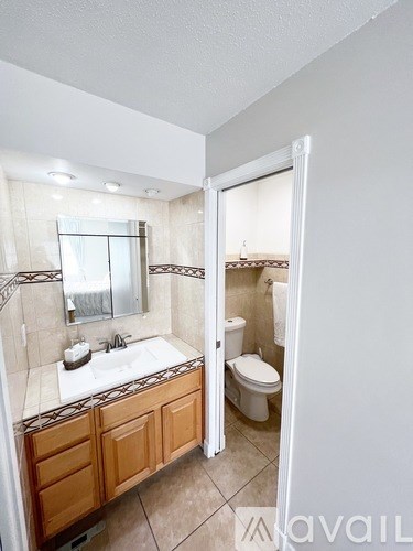 A bathroom with a sink, mirror, toilet and wooden cabinets.