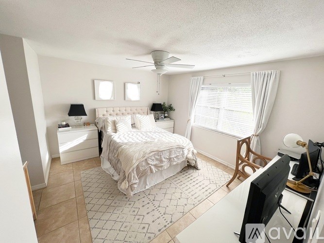 A bedroom with a large bed, a TV, and a window with white curtains.