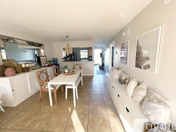A well-lit, spacious living room with a dining area and kitchen in the background.