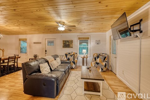 A living room with a black leather couch and wooden flooring.