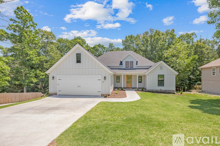 A white house with a brown roof and a garage door is surrounded by greenery.