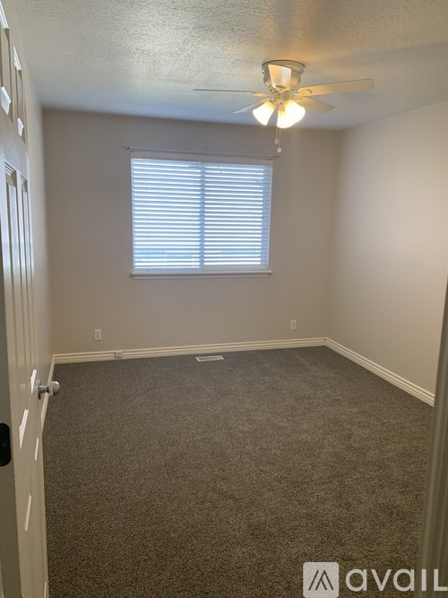 A room with a carpeted floor, a ceiling fan, and a window with blinds.