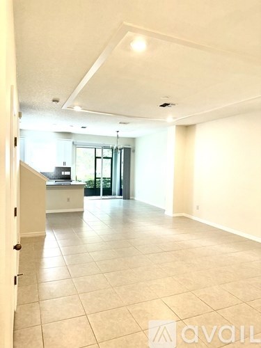 A spacious room with tiled flooring and a kitchen area in the background.