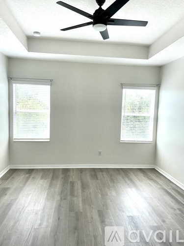 A room with a ceiling fan and two windows.