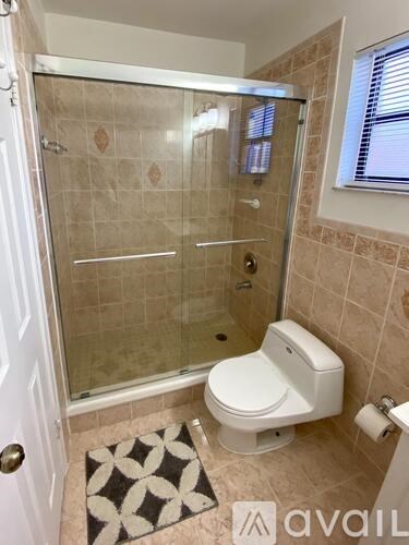 A bathroom with a toilet, a glass shower stall, and a tiled wall.