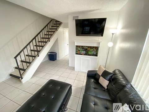 A living room with a black leather couch and a television on the wall.