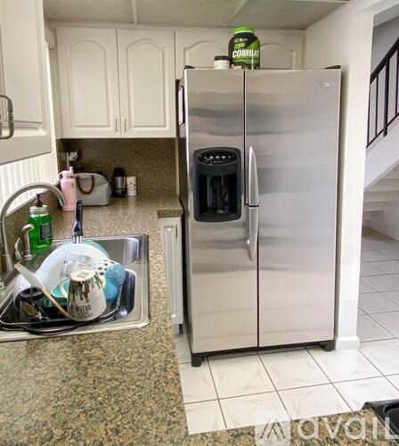 A kitchen with a stainless steel refrigerator and a sink full of dishes.