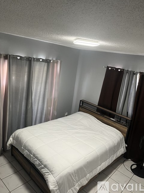 A bedroom with a bed, a mirror, and a window with curtains.