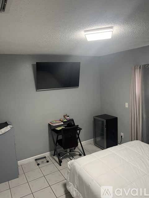 A bedroom with a bed, desk, chair, and a television mounted on the wall.
