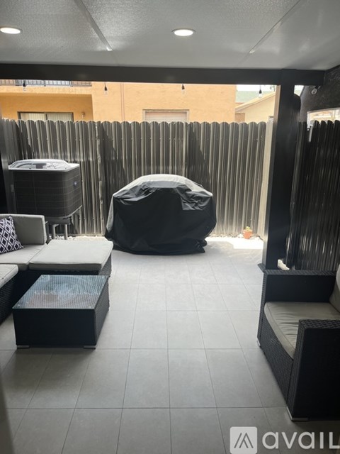 A patio with a black wicker sofa, a black ottoman, and a black umbrella.
