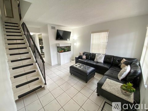 A living room with a black couch and a staircase.
