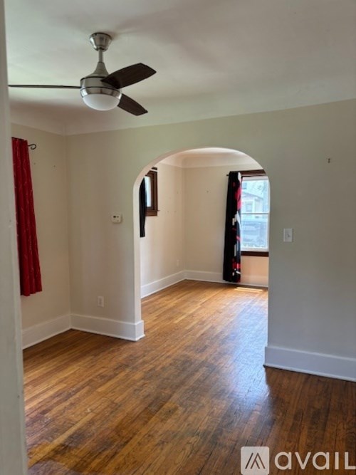 A room with a fan and a window with red curtains.