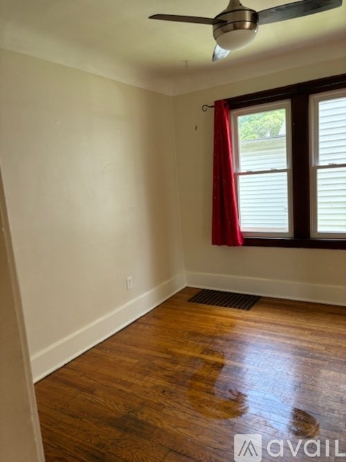 A room with a ceiling fan and a window with red curtains.