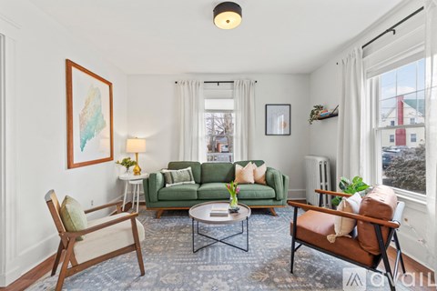 A living room with a green couch, a wooden chair, and a brown chair.