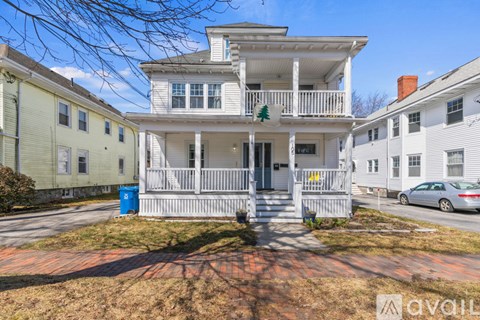A white two-story house with a balcony and a blue trash can in front.