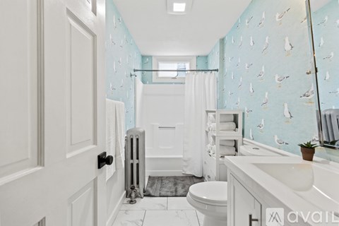 A bathroom with a white toilet, sink, and a blue wallpaper with birds on it.