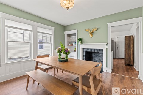 A wooden table with a vase of flowers on it sits in a room with a fireplace and a moose head on the wall.