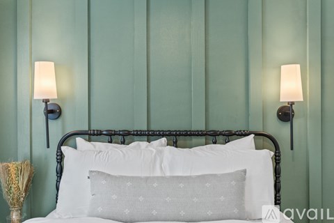 A bed with a metal headboard and white pillows is in front of a green wall.
