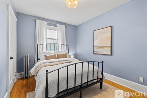 A bedroom with a bed, pillows, a window with curtains, a lamp, and a painting on the wall.