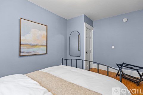 A bedroom with a bed, a mirror, and a painting on the wall.