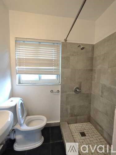 A bathroom with a toilet, a shower, and a window with blinds.