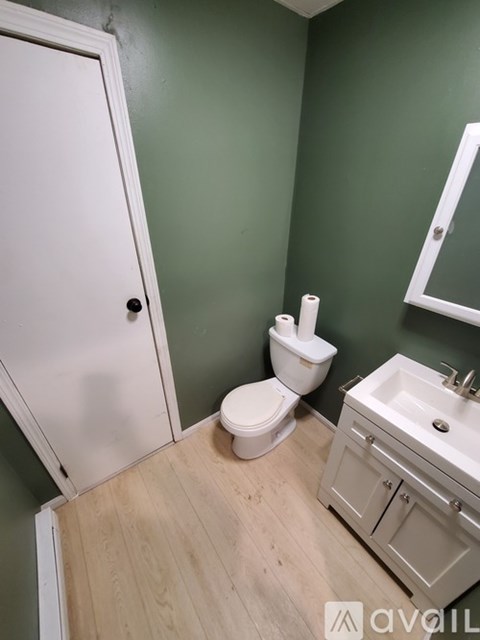 A bathroom with green walls, a white toilet, a sink, and a white door.