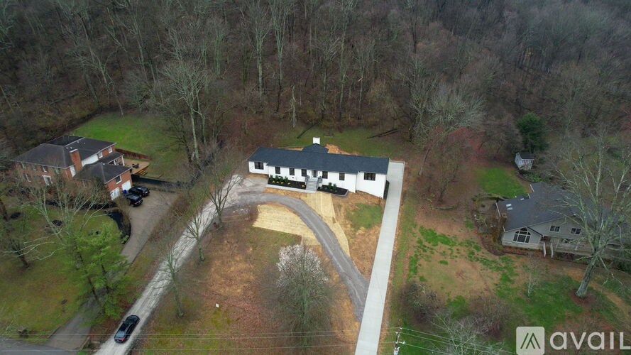 A large white building with a black roof is surrounded by a grassy area and trees.