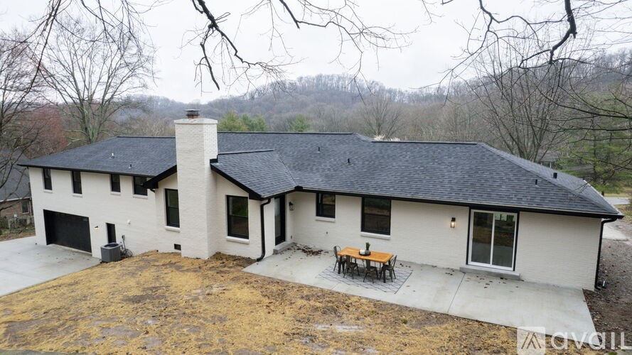 A house with a black roof and a chimney is surrounded by trees.