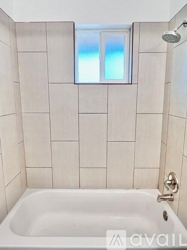 A white bathtub in a bathroom with a window above it.