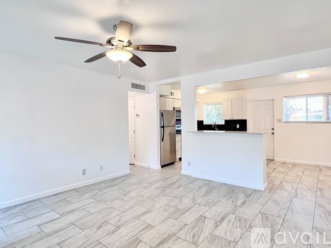 A spacious living room with a ceiling fan and a kitchen area in the background.