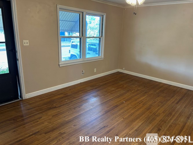 A room with wooden flooring and a window showing a view of a car and a building.