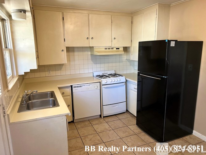 A kitchen with a black refrigerator, white cabinets, and a white dishwasher.