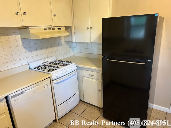 A kitchen with a black refrigerator, white dishwasher, and white oven.