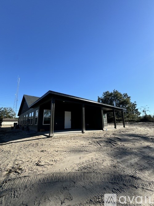 A small building with a black roof and white walls is situated on a sandy area.