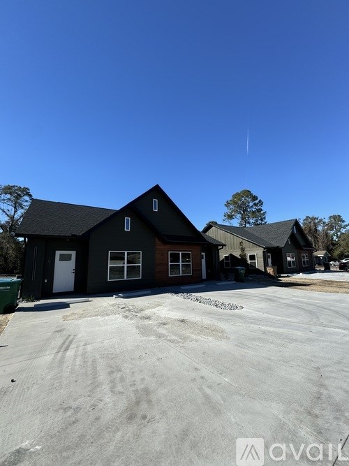 A house with a black roof and white door is surrounded by a gravel lot.