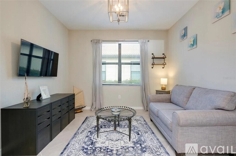 A living room with a grey couch, a black dresser, a TV, and a window with curtains.