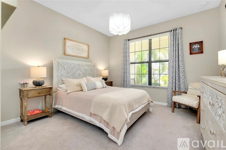 A bedroom with a large bed, a window with curtains, and a nightstand with a lamp.