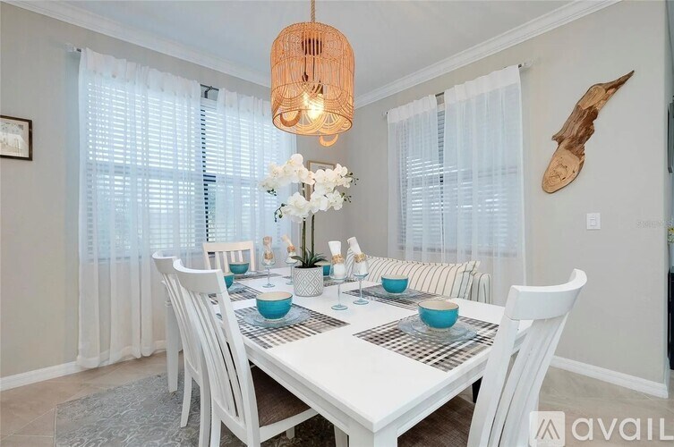 A dining room with a white table and chairs, a hanging light fixture, and a decorative piece on the wall.