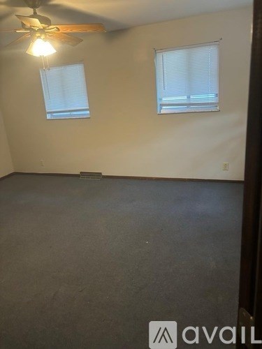 A room with a ceiling fan and two windows.