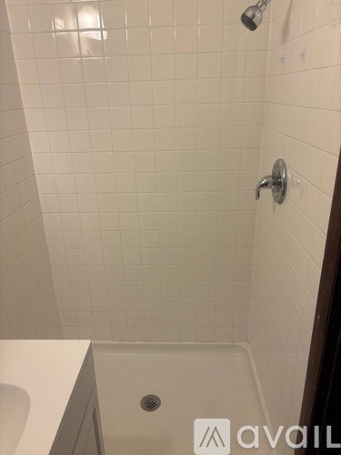 A white tiled shower area with a drain in the middle.