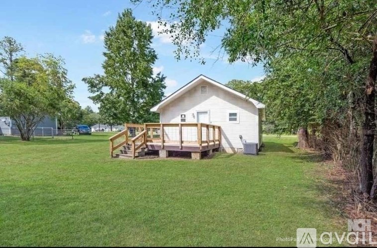 A white house with a deck in the middle of a grassy area.